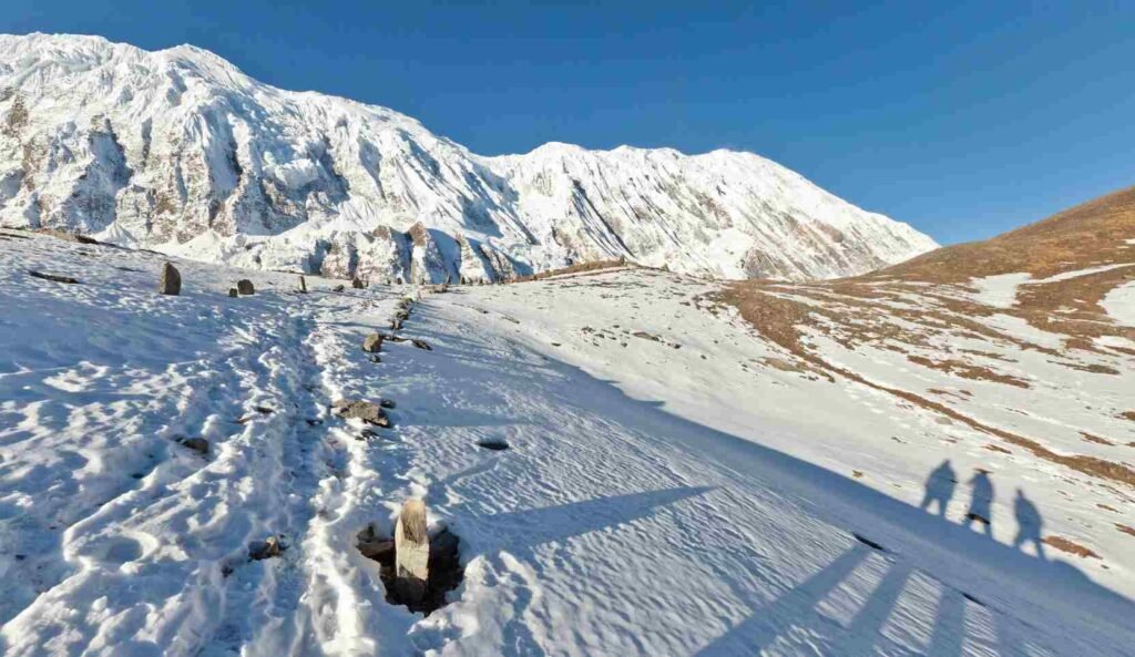 a group of three person taking picture of trail covered with snow enroute to Tilicho lake trek